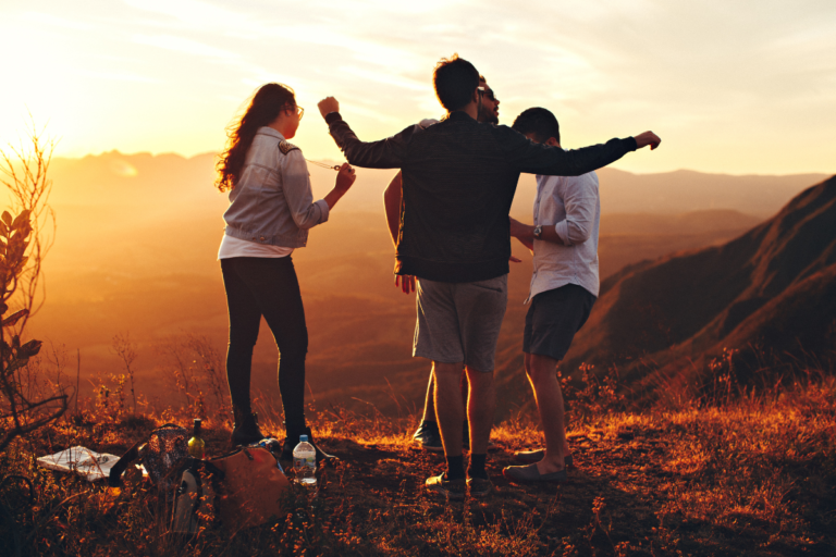 Friends celebrating on a mountain viewpoint at sunset, representing connection, adventure, and meaningful travel experiences.
