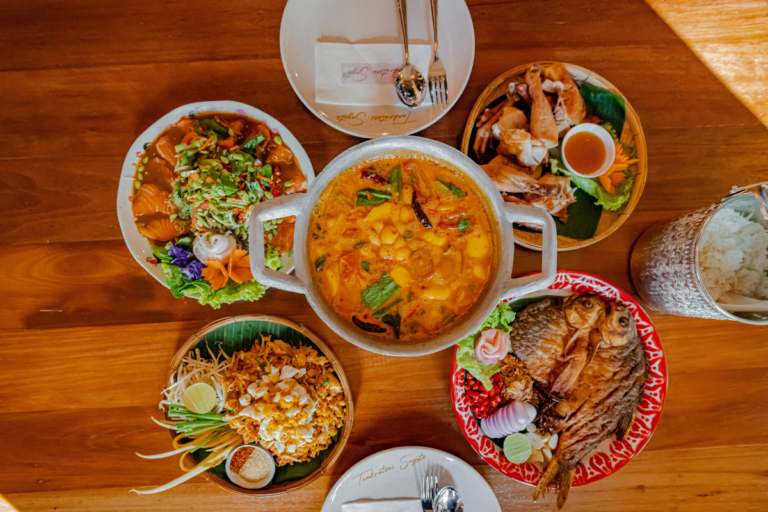 Traditional Thai meal spread featuring tom yum soup, pad thai, grilled fish, and fresh seafood dishes on a wooden table.