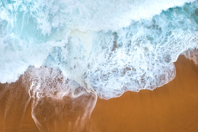 Aerial view of ocean waves meeting a sandy beach, symbolizing travel, exploration, and the calming benefits of traveling.