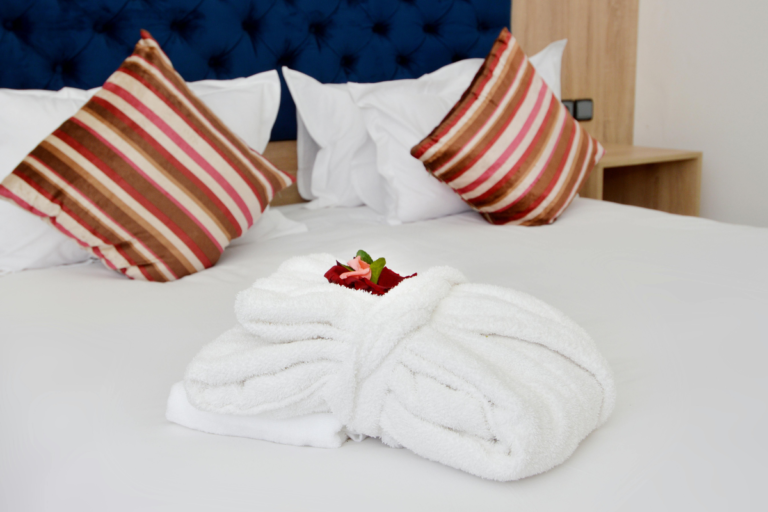 Cozy and neatly prepared bedroom with soft white linens, decorative pillows, and folded towel accents for a relaxing travel stay.